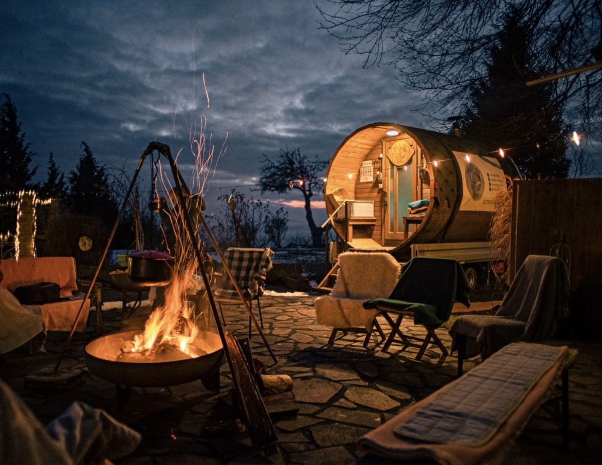 Fasssauna bei Nacht mit Feuerstelle und Lichterketten